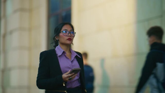 A confident business woman walks through an urban environment, engaged with her smartphone. She navigates the city while checking her mobile device.