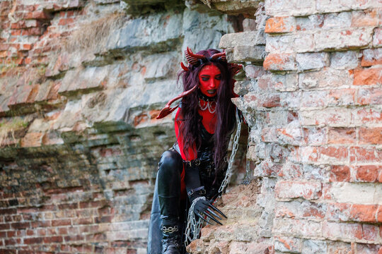 Demonic cosplay woman with horns and chains posing on old brick wall