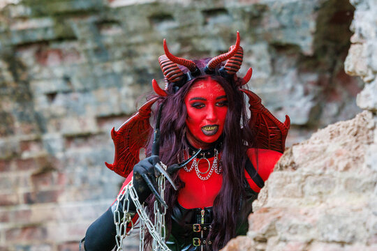Demonic cosplay woman with horns and chains posing on old brick wall