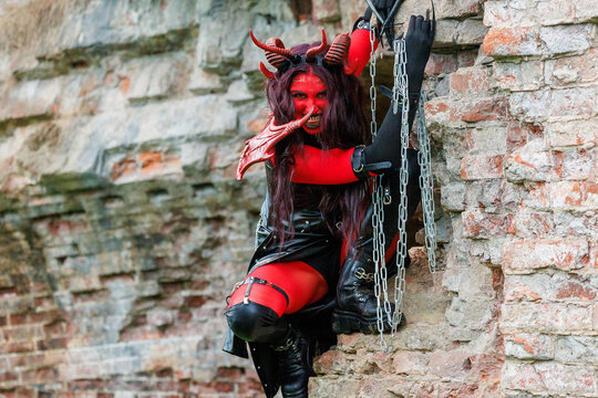 Demonic cosplay woman with horns and chains posing on old brick wall