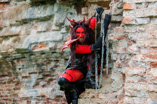 Demonic cosplay woman with horns and chains posing on old brick wall