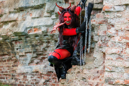 Demonic cosplay woman with horns and chains posing on old brick wall
