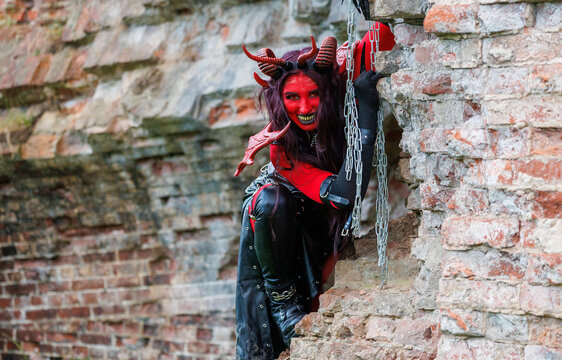 Demonic cosplay woman with horns and chains posing on old brick wall