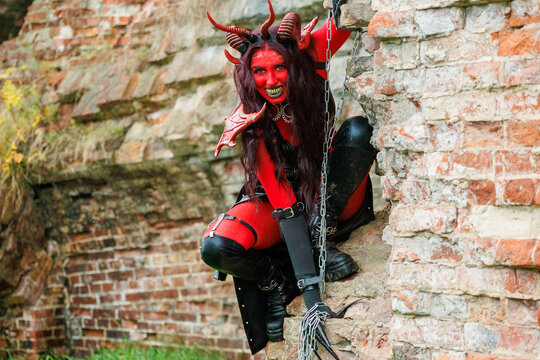 Demonic cosplay woman with horns and chains posing on old brick wall