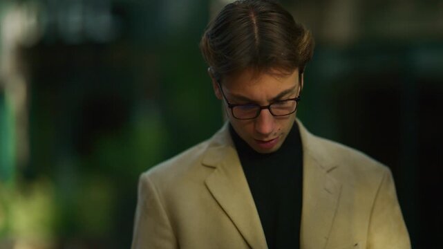 A focused young man in glasses checks his wristwatch in an urban setting. He appears to be waiting and confirming the time.