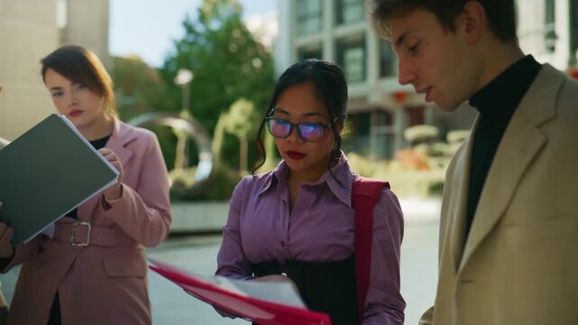 Young business professionals engage in an outdoor discussion, reviewing important documents. A diverse team collaborates on a project in a modern urban environment.