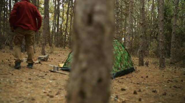 Woman enters a camouflage tent while the couple camps in a pine forest and the man moves around the campsite.