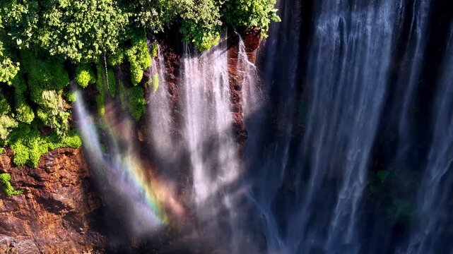Waterfalls cascade over mossy rocks, creating mist at Tumpak Sewu
