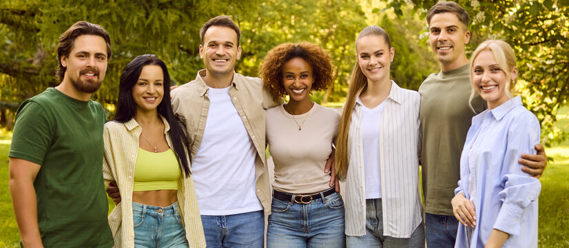 Friends group smiling outdoors shows unity togetherness. Seven young adults pose together in park, showing diverse community and belonging. Celebrating youth connection, teamwork and friendship.