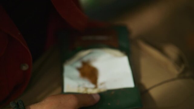 Man seals loose tobacco in rolling paper to make a hand rolled cigarette, then closes and ties a leather tobacco pouch.