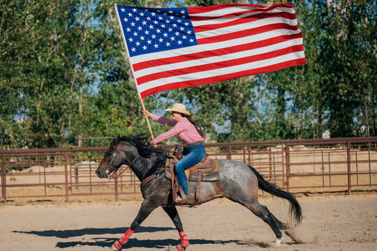 Cowgirl galloping on horseback waving american flag