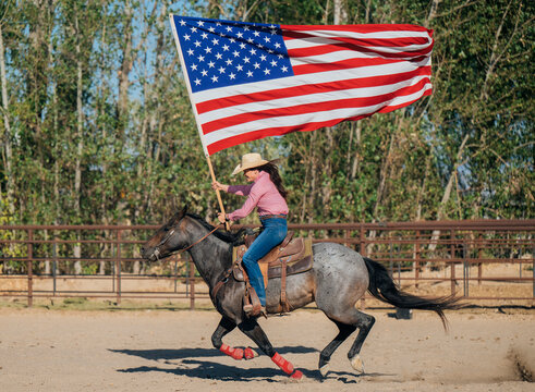 White woman riding horse while carrying american flag in outdoor arena