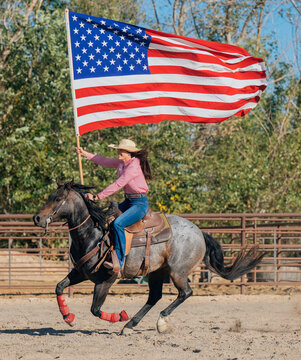 Female rider galloping horse carrying american flag in rodeo arena
