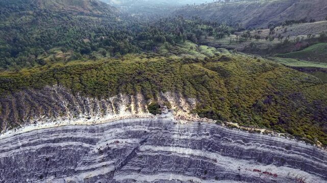 Aerial view of a starkly striped mountain slope. Felled trees line the edge of the scarred earth at Mount Ijen