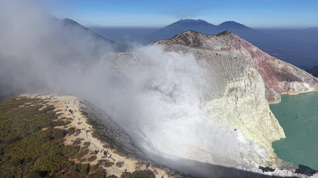 Expansive aerial view of active volcanic crater. White smoke billows from the crater opening at Mount Ijen