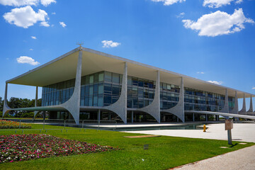 Obraz premium Exterior view of the iconic Palácio do Planalto government building with modernist architectural columns under a bright blue sky with white clouds in Brasilia, Brazil