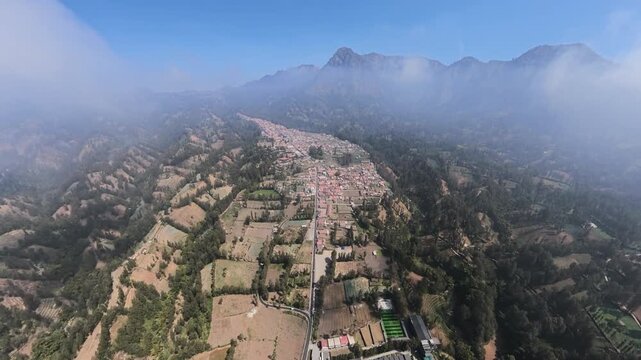 High altitude drone fisheye view of Cemoro Lawang village, valley farmland and misty volcanic peaks