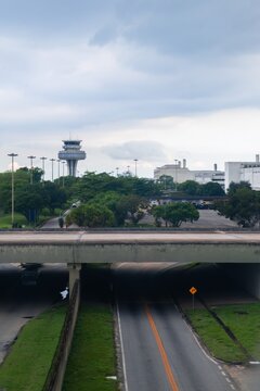 Rio de Janeiro, Brazil - 18 October 2026: View of RIOgaleao International Airport, featuring its control tower, lush greenery, and an overpass bridge under a cloudy sky.