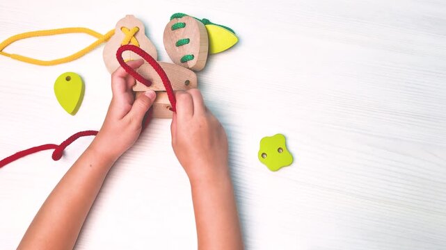 Close up of child hands threading lace through wooden toy fruit Educational video clip demonstrating fine motor skills development 4k resolution Hands eyes coordination Montessori sensorial activity