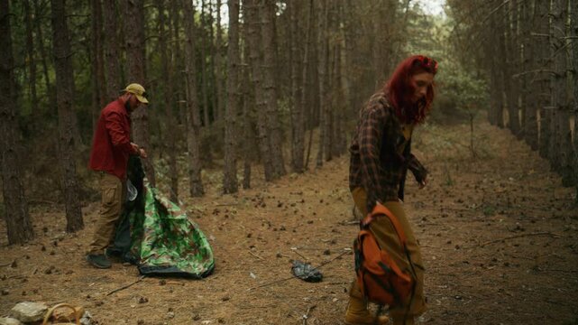 Couple arranges camping gear while setting up a camouflage tent during a forest camping trip.