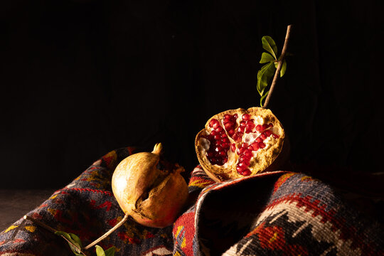 Natura morta artistica con melagrane intere e aperte su tappeto kilim, illuminate in chiaroscuro