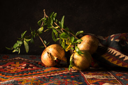 Natura morta artistica con melagrane intere e aperte su tappeto kilim, illuminate in chiaroscuro