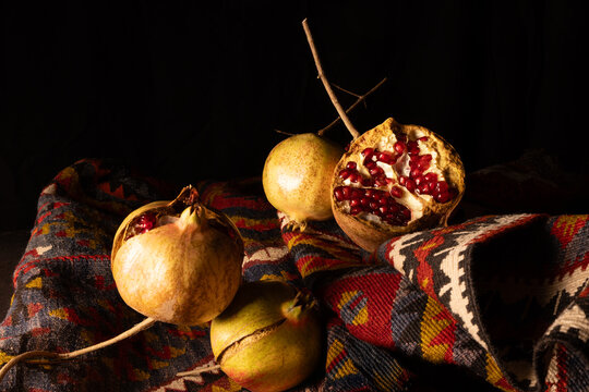 Natura morta artistica con melagrane intere e aperte su tappeto kilim, illuminate in chiaroscuro