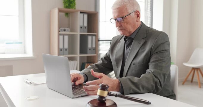 Senior judge works on laptop beside gavel. Professional examines daily paperwork for legal counsel, court administration, and justice services. Legal expertise guides informed decisions.