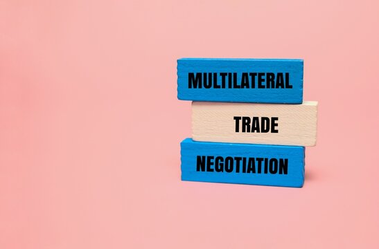 Stacked colored wooden blocks with "MULTILATERAL TRADE NEGOTIATION" text on a pink background. International business strategy, global commerce, and economic agreement concepts