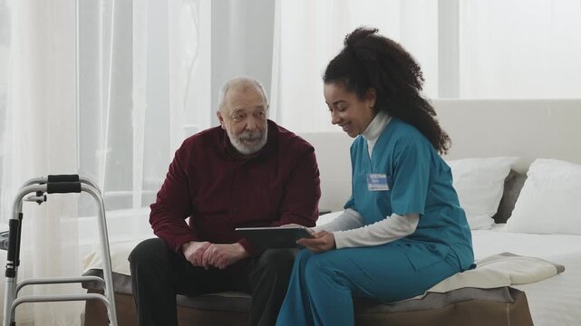 Kind Black caregiver teaches elderly man how to use modern apps on tablet