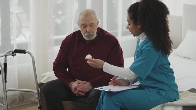African American female doctor hands pill bottle to senior man in nursing home