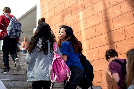 Students with backpacks walking up stairs near a brick wall.