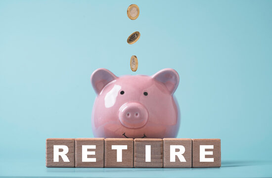 Retirement savings and financial planning concept with pink piggy bank receiving falling coins behind wooden RETIRE blocks for pension funds, financial security and future wealth goals.