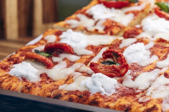 Delicious freshly baked Italian pizza topped with melted mozzarella, creamy burrata, roasted tomatoes and fresh basil leaves, close-up.