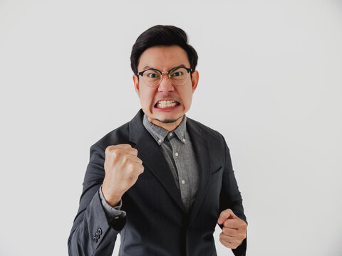 Young Asian businessman clenches his fists and gritting teeth, expressing intense anger and frustration.
