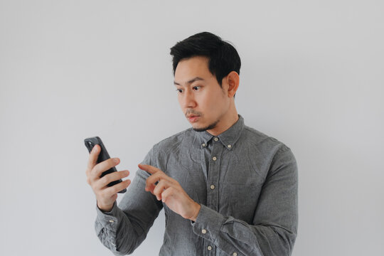 Young Asian Man in Grey Shirt Looking Intently at His Smartphone with a Surprised Expression