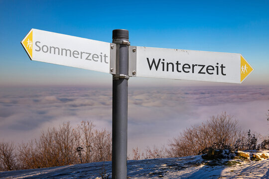 Richtungspfeile vor klarem, tiefblauem Himmel &uuml;ber einer Wolkendecke zeigen in die Richtungen Sommerzeit und Winterzeit