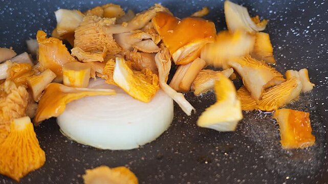 Close-up video of golden chanterelle mushrooms frying beside a thick slice of white onion in a nonstick pan