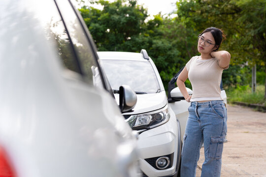 A young woman touches her neck beside two white cars in an outdoor parking area, offering a conceptual image for vehicle incidents, personal injury, and insurance coverage.