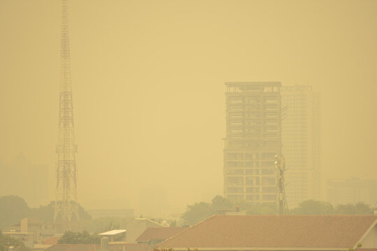High-angle landscape photograph showing a dense layer of yellowish haze and toxic smog blanketing a city landscape, obscuring skyscrapers, residential buildings