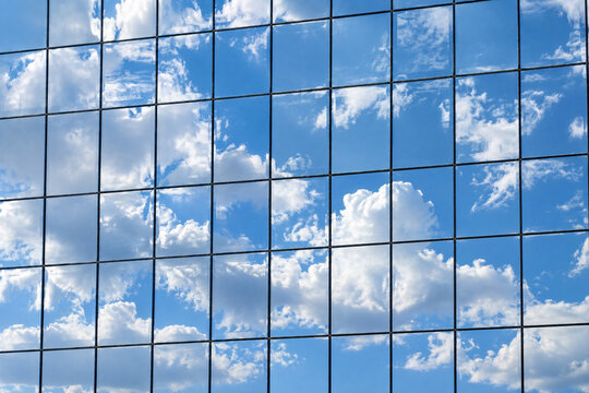 Glass curtain wall of an office building mirroring white clouds and blue sky in a grid of square panes