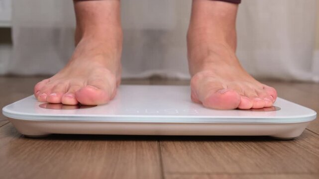 Close-up of woman bare foot stepping onto digital bathroom scale on wooden floor. Weight control and diet concept. Healthy lifestyle and body measurement for fitness tracking at home