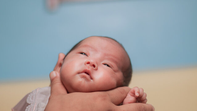 Infant care concepts, newborn, cradle the head, tenderness, and early family bonding. Close up portrait newborn baby gently supported adult hand, wearing white outfit against warm pastel background.
