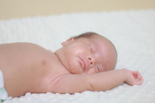 Close up newborn baby, infant, sleeping peacefully on a soft white blanket, quiet moment of rest, comfort, and early infant development.