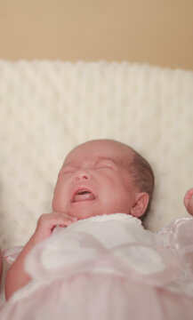 Newborn baby crying while being gently supported by a parent's hand, wearing a white outfit, authentic moment of infant emotion, parental comfort, and early childcare.