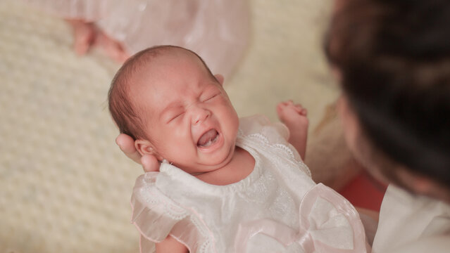 Newborn baby crying while being gently supported by a parent's hand, wearing a white outfit, authentic moment of infant emotion, parental comfort, and early childcare.