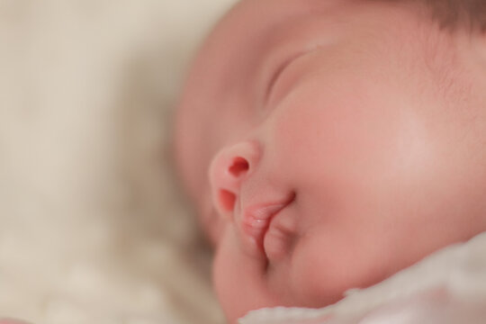 Close up newborn baby, infant, sleeping peacefully on a soft white blanket, quiet moment of rest, comfort, and early infant development.
