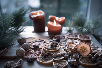 Christmas still life with dried citrus fruits, spices, and nuts on wooden surface, accompanied by candles. © gudrun