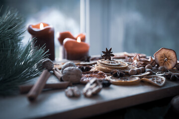 Christmas still life with dried citrus fruits, spices, and nuts on wooden surface, accompanied by candles. © gudrun