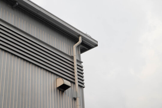 Low angle view of modern warehouse roof edge with rain downspout pipe and exhaust wall cap.